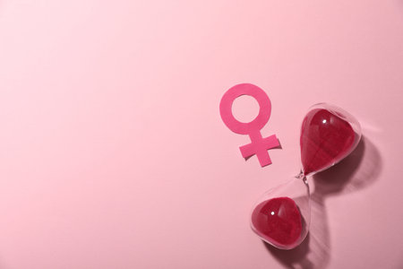 Menopause. Female gender symbol and hourglass on pink background, top view. Space for text