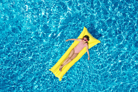 Girl on inflatable mattress in swimming pool, top view. Summer vacationの写真素材