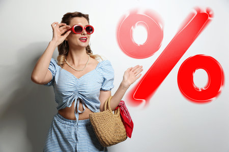 Fashionable woman with bag looking at percent sign against white background