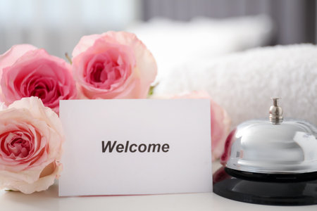 Card with Welcome word, desk bell, roses and towel on white table, closeupの写真素材