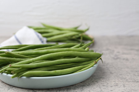 Fresh green bean pods on gray textured table, closeup.
