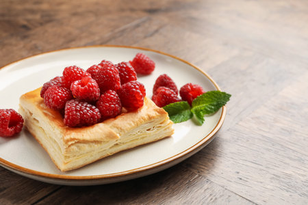 Yummy puff pastry with raspberries on wooden table, closeup