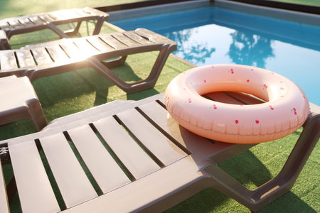 Pink inflatable ring on sun lounger near swimming pool outdoors, space for text