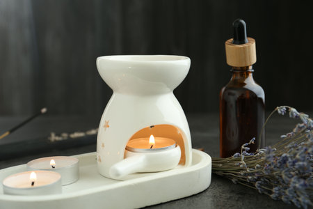 Aroma lamp with burning candles, dropper and lavender on gray textured table against black background, closeupの写真素材