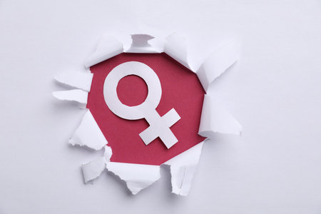 Menopause. Female gender symbol on crimson background, view through hole in torn white paperの写真素材