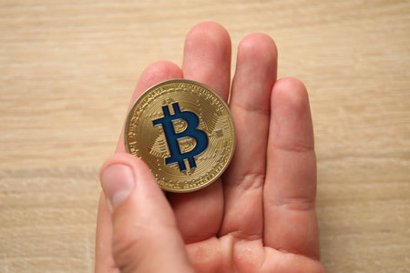 Cryptocurrency. Man with golden bitcoin at wooden table, closeupの写真素材
