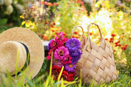 Bouquet of flowers in bag and wicker hat on green grass outdoorsの写真素材