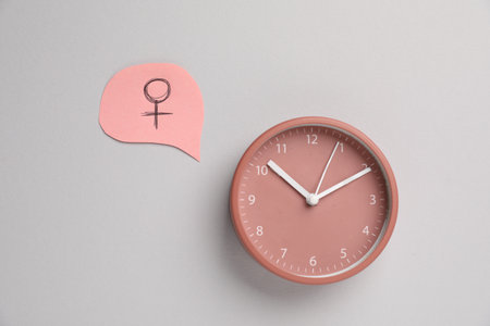 Menopause. Female gender symbol and alarm clock on light gray background, flat layの写真素材