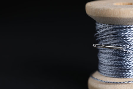 Spool of blue thread with sewing needle on black background, macro view. Space for text