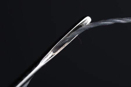 Sewing needle with thread on black background, macro view