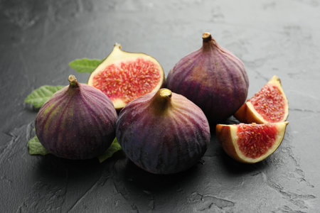 Whole and cut figs on dark textured table, closeup