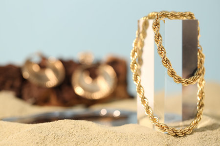 Beautiful gold chain on sand, closeup. Space for text