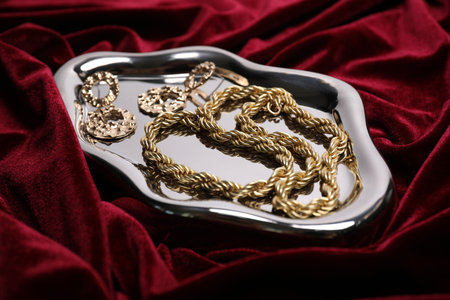 Stylish gold jewelry on red cloth, closeup