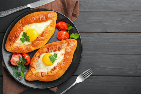 Tasty khachapuri with cheese and eggs served on black wooden table, flat lay. Space for text