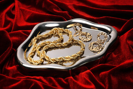 Stylish gold jewelry on red cloth, closeup