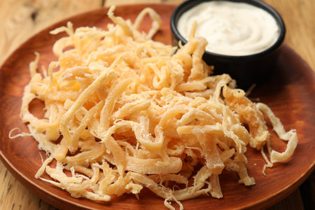 Tasty dried squid shavings and sauce on wooden table, closeup