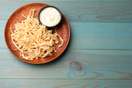 Tasty dried squid shavings and sauce on light blue wooden table, top view. Space for text