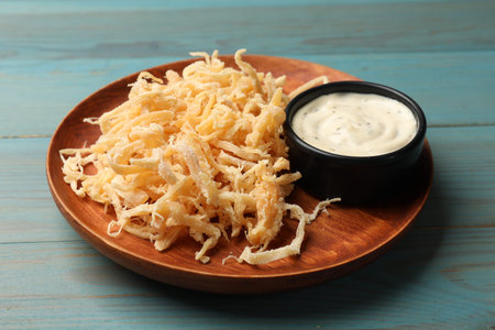 Tasty dried squid shavings and sauce on light blue wooden table, closeup