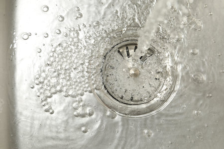 Stream of water going into sink drain, closeup