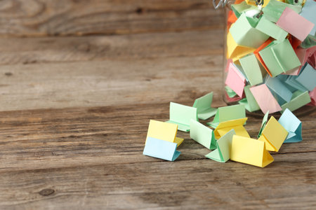 Colorful paper pieces in glass jar on wooden table, closeup. Space for text. Notes with messages