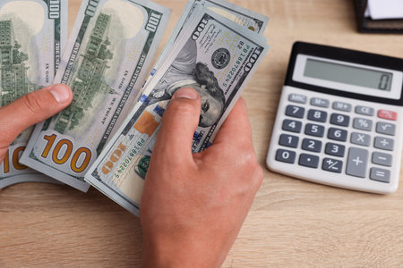 Man counting dollar banknotes at wooden table, closeup