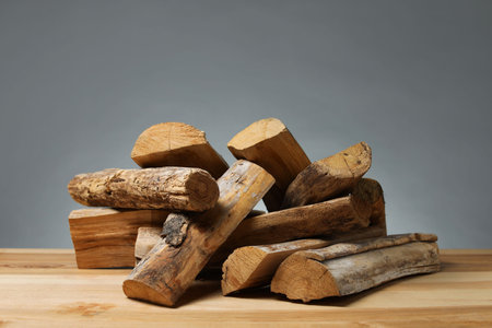 Pile of cut firewood on wooden table against gray background