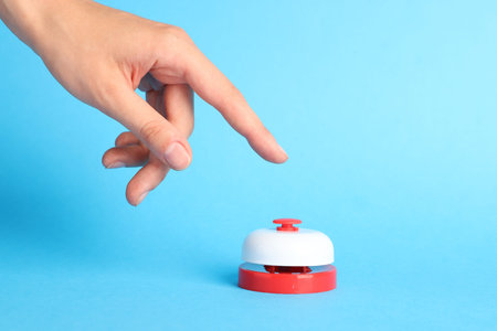 Hand pressing red button on light blue background, closeup