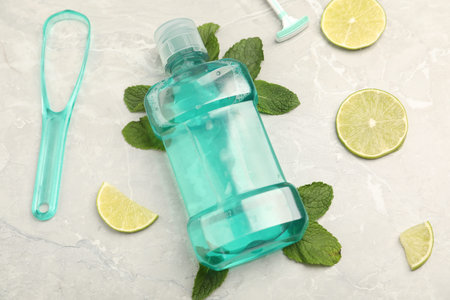 Mouthwash, other oral hygiene products, mint and lime slices on light marble table, closeup