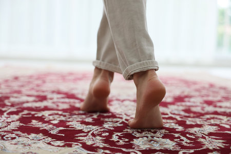 Woman walking barefoot on red carpet with pattern at home, closeup