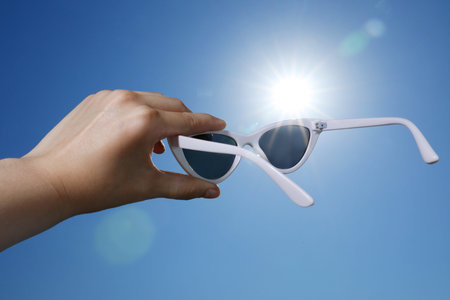 Woman holding sunglasses against blue sky on sunny day, low angle view
