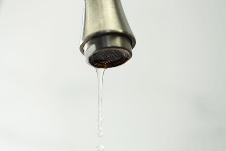 Water saving concept. Water dripping from tap on light background, closeup