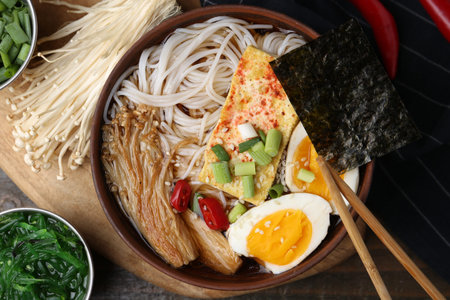 Tasty ramen with enoki mushrooms in bowl on table, flat lay