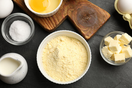 Cornbread preparation. Different ingredients on black textured table, flat lay