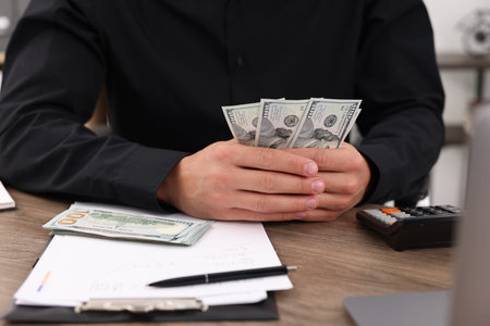 Man counting dollar banknotes at wooden table, closeup