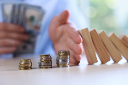 Risk. Man with dollars stopping domino effect to protect coins at table, closeup