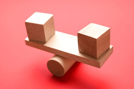 Risk. Wooden seesaw scale with cubes on red background, closeup