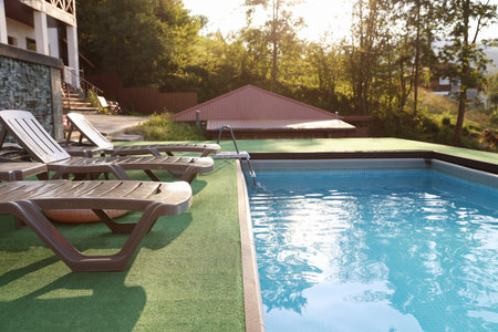 Empty sun loungers on artificial grass near outdoor swimming pool