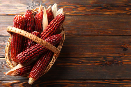 Ripe red corn cobs in basket on wooden table, top view. Space for textの写真素材