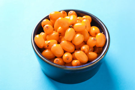 Ripe sea buckthorn berries in bowl on light blue background, closeupの写真素材