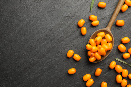 Fresh sea buckthorn berries, spoon and leaves in on black table, flat lay. Space for text