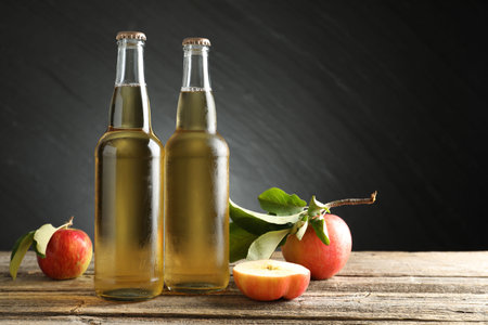 Cider in glass bottles and apples on wooden table against dark gray background. Space for textの写真素材