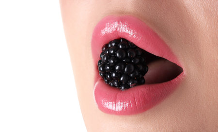 Woman with pink lipstick on her lips and blackberry against white background, closeup