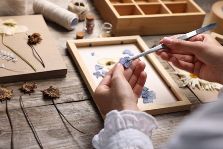 Woman putting dry flowers into picture frame at wooden table, closeupの写真素材