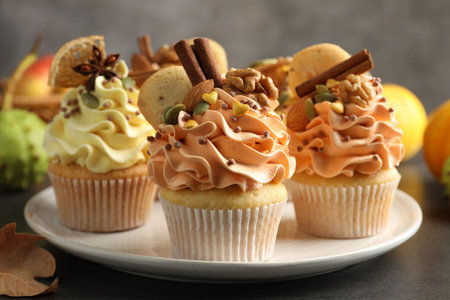 Delicious cupcakes with colorful cream, spices, nuts and autumn decor on gray table, closeupの写真素材