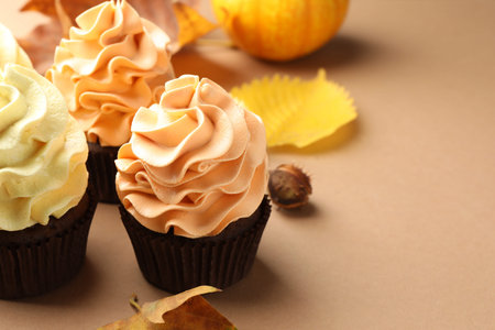 Delicious cupcakes with colorful cream and autumn decor on beige background, closeup. Space for textの写真素材