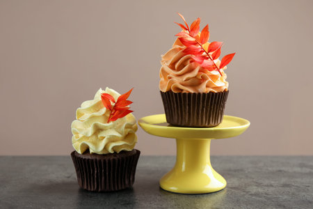 Delicious cupcakes with branches with red leaves on gray textured table, closeup. Autumn atmosphereの写真素材