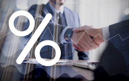 Business partners shaking hands, multiple exposure with buildings, percent sign and graphの写真素材