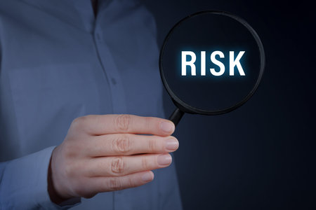 Woman holding magnifying glass with the word Risk inside against dark background, closeup