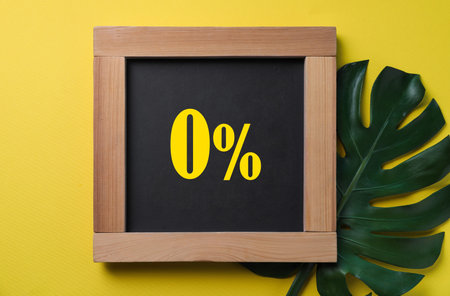 Chalkboard with 0% and green leaf on yellow background, top view