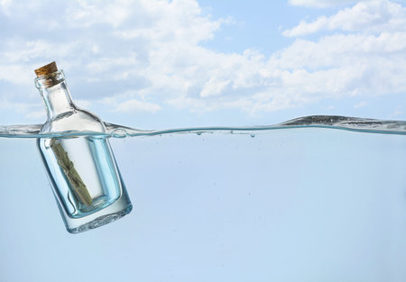 Corked bottle with rolled letter in water under skyの写真素材